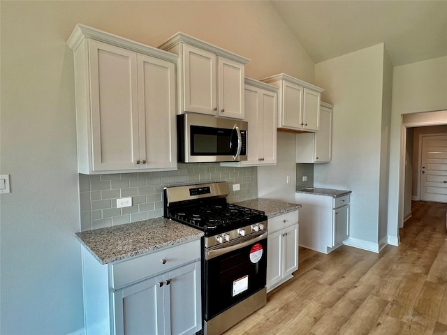 kitchen featuring vaulted ceiling, light stone countertops, white cabinets, and appliances with stainless steel finishes