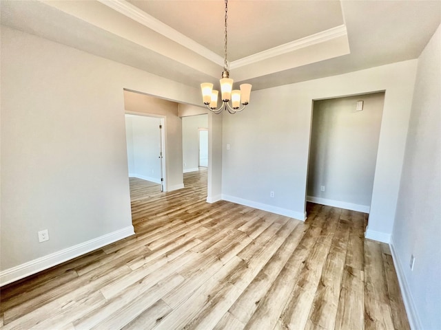 unfurnished dining area with an inviting chandelier, ornamental molding, a raised ceiling, and light wood-type flooring