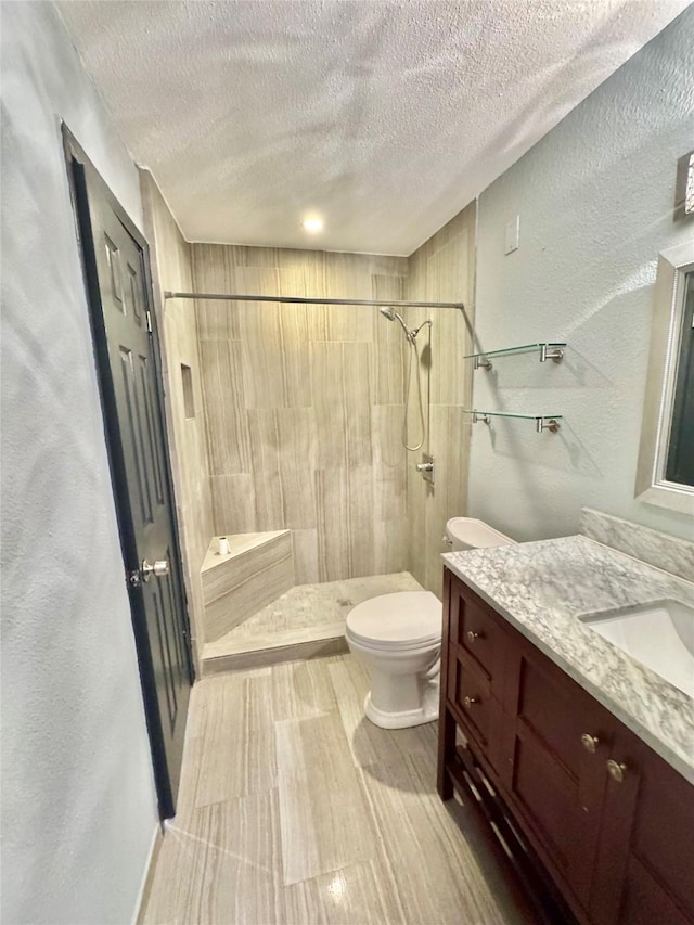 bathroom with vanity, tiled shower, a textured ceiling, and toilet