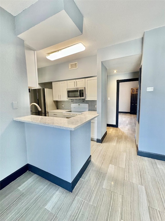 kitchen featuring white cabinets, backsplash, kitchen peninsula, stainless steel appliances, and light stone countertops