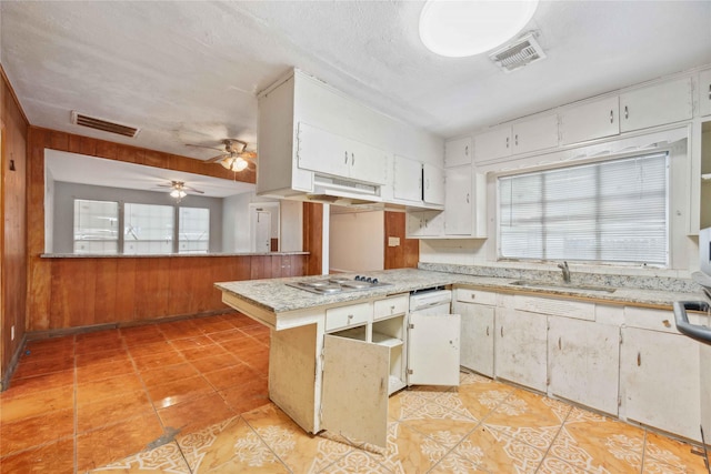 kitchen featuring sink, stainless steel gas cooktop, white cabinets, kitchen peninsula, and wood walls