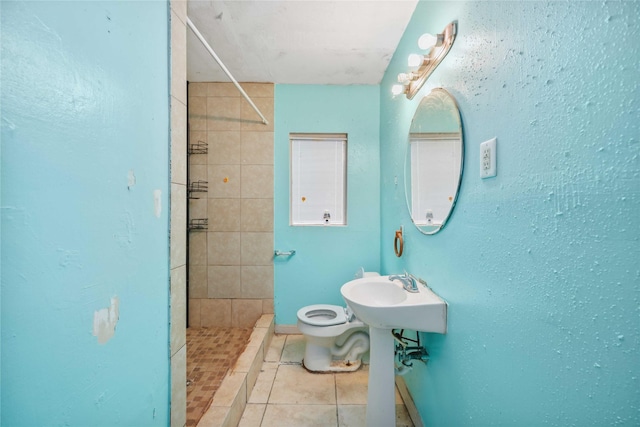 bathroom with tile patterned flooring, tiled shower, sink, and toilet