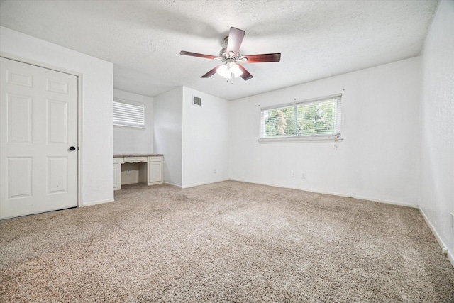 unfurnished bedroom featuring ceiling fan, built in desk, carpet, and a textured ceiling