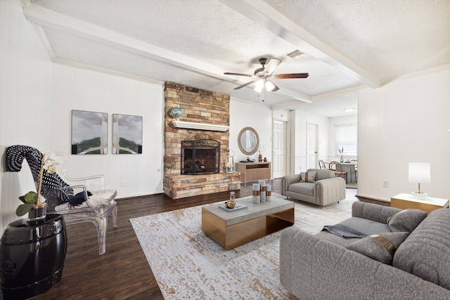 living room featuring beamed ceiling, a stone fireplace, dark wood-type flooring, and a textured ceiling