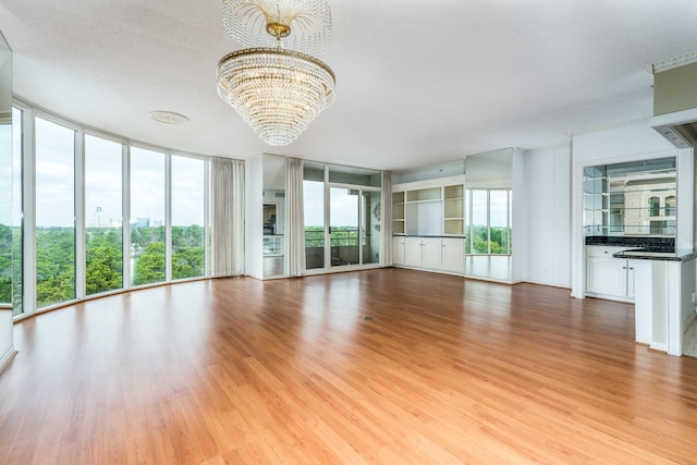 unfurnished living room featuring an inviting chandelier, a wall of windows, light hardwood / wood-style flooring, and a textured ceiling