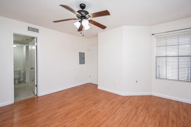 unfurnished room with ceiling fan, electric panel, light hardwood / wood-style flooring, and a textured ceiling