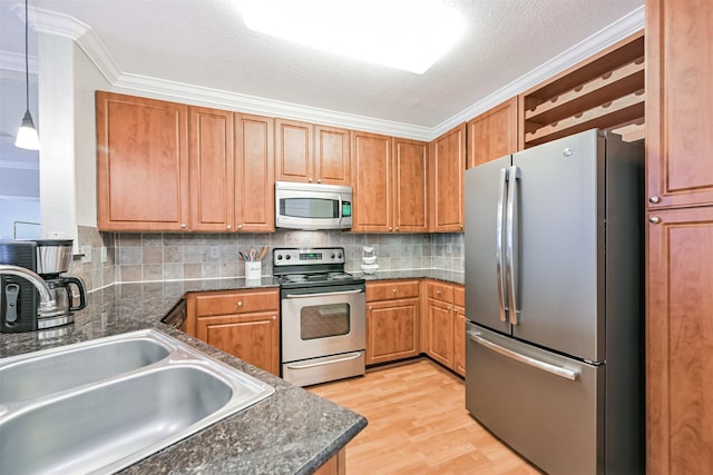 kitchen with appliances with stainless steel finishes, sink, hanging light fixtures, crown molding, and light wood-type flooring