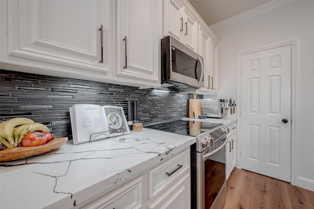 kitchen featuring appliances with stainless steel finishes, light stone countertops, white cabinets, decorative backsplash, and ornamental molding