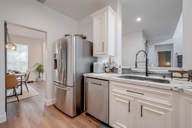 kitchen with appliances with stainless steel finishes, light hardwood / wood-style flooring, light stone countertops, sink, and white cabinetry