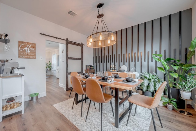 dining area with a barn door, light wood-type flooring, and a chandelier