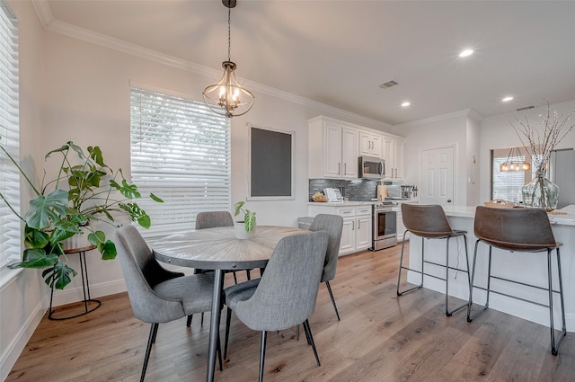 dining room featuring light wood-type flooring, crown molding, and an inviting chandelier