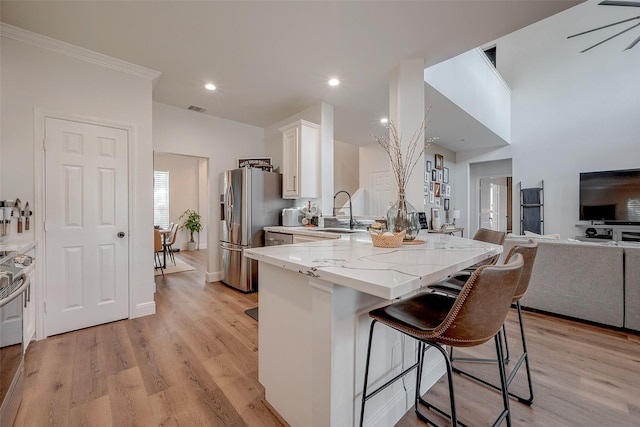 kitchen with a kitchen bar, sink, stainless steel fridge, white cabinets, and light stone countertops