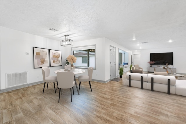 dining room with an inviting chandelier, light hardwood / wood-style floors, and a textured ceiling