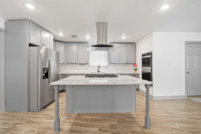 kitchen featuring stainless steel appliances, island exhaust hood, light stone countertops, and a center island