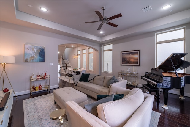 living room featuring dark wood-type flooring, ceiling fan, and a raised ceiling