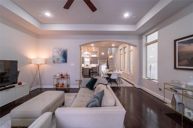 living room with plenty of natural light, dark hardwood / wood-style floors, ceiling fan, and a tray ceiling