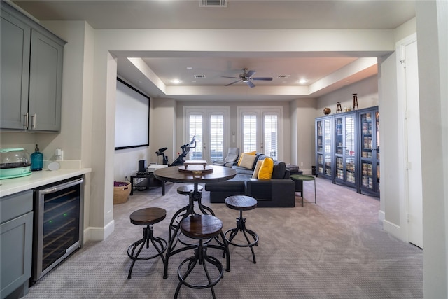 carpeted dining area with a raised ceiling, bar area, beverage cooler, and french doors