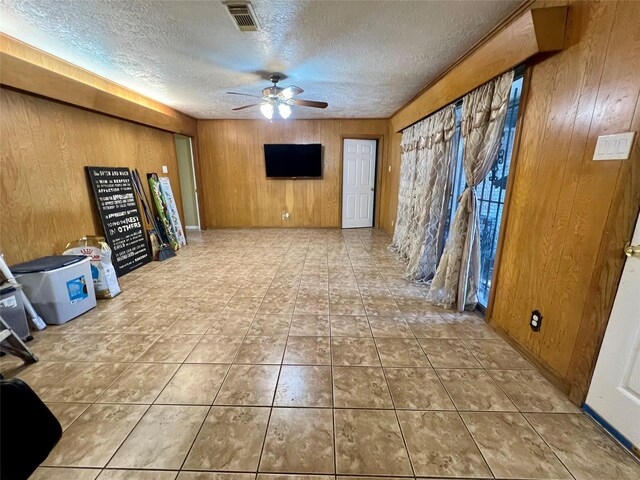 unfurnished living room featuring tile patterned flooring, a textured ceiling, ceiling fan, and wood walls