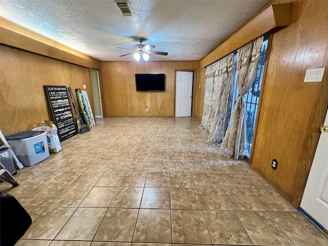 unfurnished living room with ceiling fan, a textured ceiling, tile patterned flooring, wooden walls, and visible vents