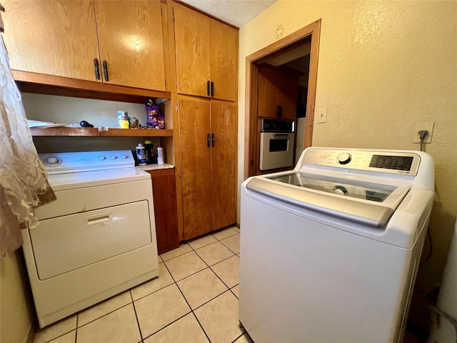 laundry room featuring light tile patterned flooring, cabinets, a textured ceiling, and washing machine and clothes dryer