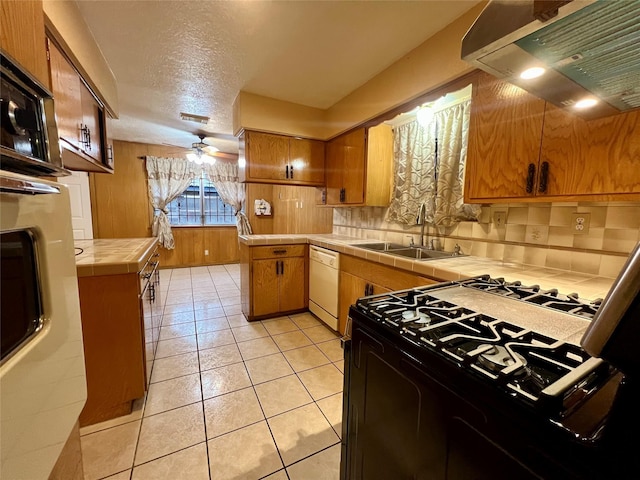 kitchen featuring tile countertops, a sink, range hood, dishwasher, and gas range