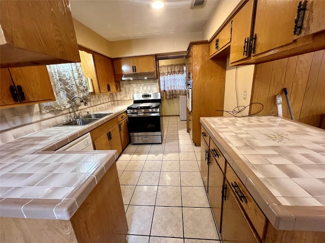 kitchen featuring tile countertops, stainless steel gas range, light tile patterned floors, and a sink