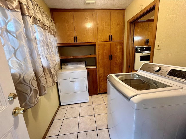 clothes washing area with cabinet space, light tile patterned floors, a textured ceiling, and washing machine and clothes dryer