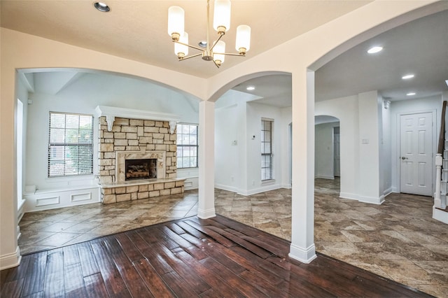 unfurnished living room featuring dark wood-type flooring, a stone fireplace, and a notable chandelier