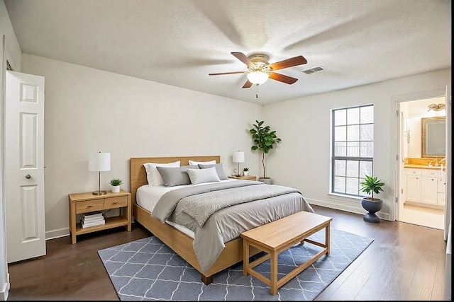 bedroom featuring ceiling fan, ensuite bath, dark wood-type flooring, and a textured ceiling