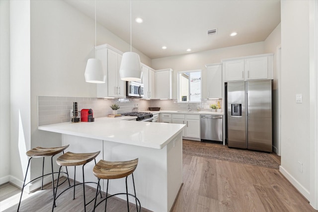 kitchen featuring light wood-style flooring, a peninsula, visible vents, appliances with stainless steel finishes, and a sink