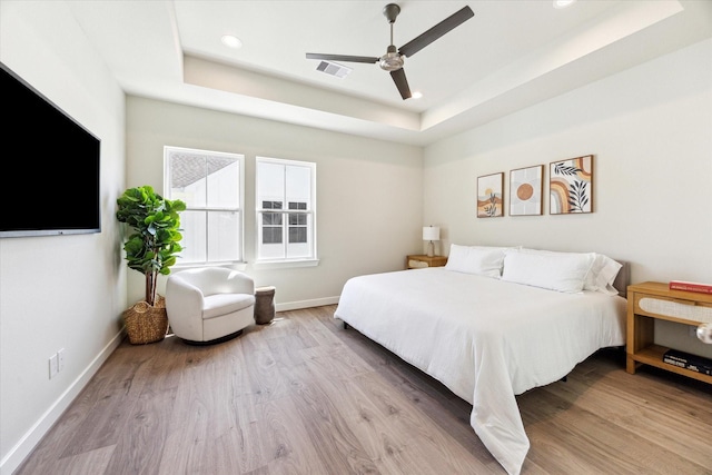 bedroom featuring visible vents, baseboards, a tray ceiling, and wood finished floors
