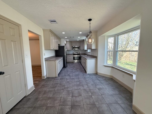 kitchen featuring appliances with stainless steel finishes, sink, hanging light fixtures, dark tile patterned floors, and a textured ceiling