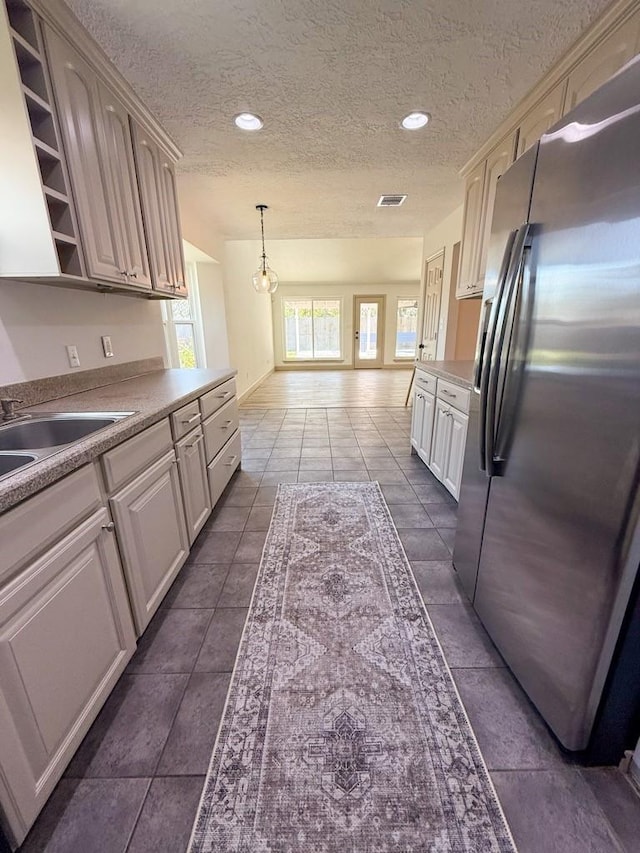 kitchen featuring stainless steel refrigerator with ice dispenser, sink, hanging light fixtures, a textured ceiling, and dark tile patterned floors