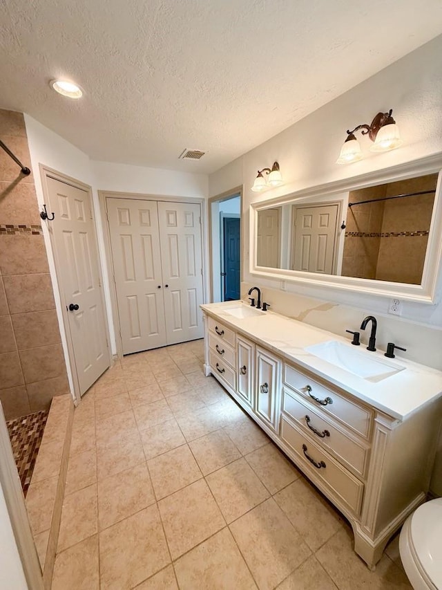 bathroom featuring vanity, tile patterned flooring, a textured ceiling, and tiled shower