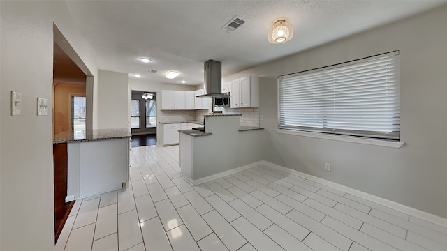 kitchen with tasteful backsplash, island range hood, kitchen peninsula, white cabinets, and dark stone counters