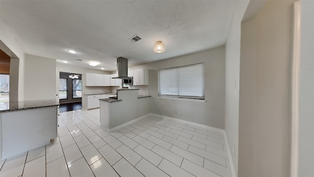 kitchen with white cabinetry, tasteful backsplash, dark stone countertops, kitchen peninsula, and island exhaust hood