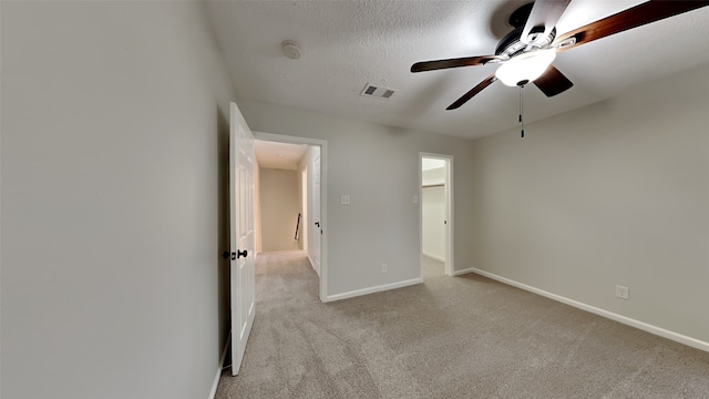 unfurnished bedroom with ceiling fan, a spacious closet, light carpet, and a textured ceiling