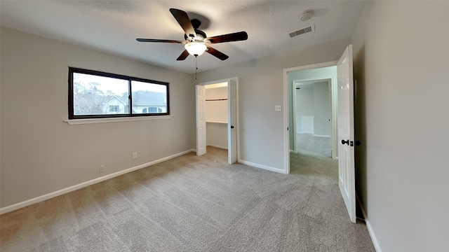 unfurnished bedroom featuring ceiling fan, a walk in closet, light carpet, and a textured ceiling