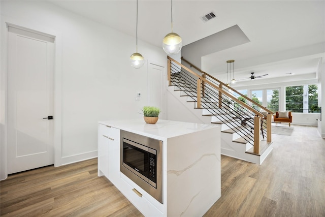 kitchen featuring light stone counters, light wood-type flooring, stainless steel microwave, pendant lighting, and white cabinets