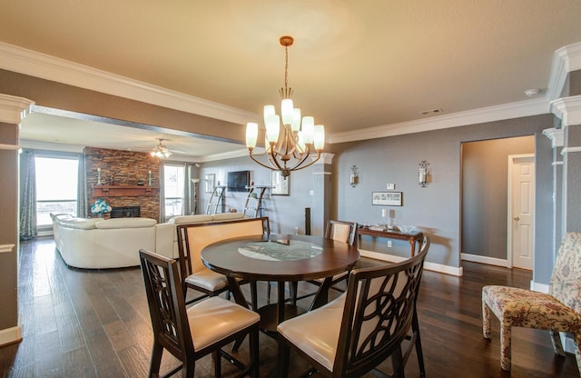 dining space featuring ornamental molding, a stone fireplace, dark hardwood / wood-style flooring, and ceiling fan with notable chandelier