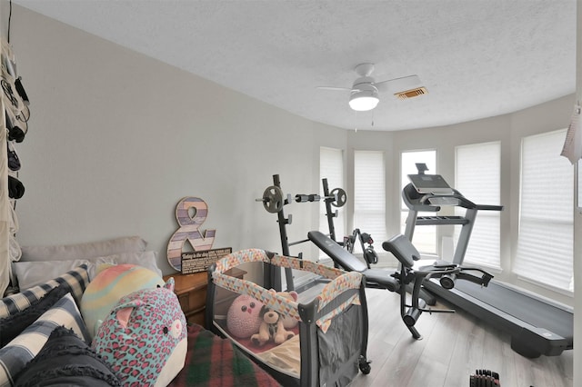 workout room with ceiling fan, a textured ceiling, and light hardwood / wood-style flooring