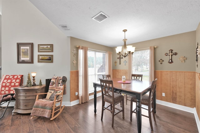 dining area with a notable chandelier, dark hardwood / wood-style floors, a textured ceiling, and wood walls