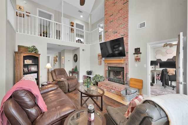 living room featuring wood-type flooring, a fireplace, ceiling fan, and a high ceiling