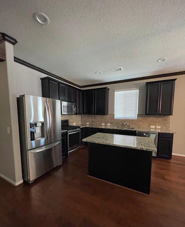 kitchen featuring dark wood-type flooring, light stone counters, appliances with stainless steel finishes, a kitchen island, and backsplash