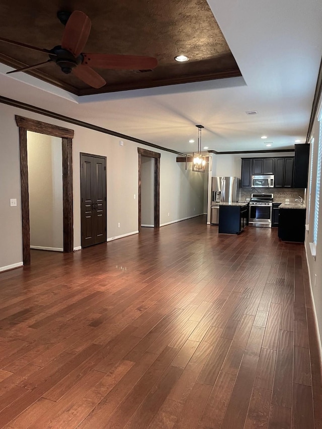 unfurnished living room with ceiling fan with notable chandelier, dark wood-type flooring, ornamental molding, and a raised ceiling