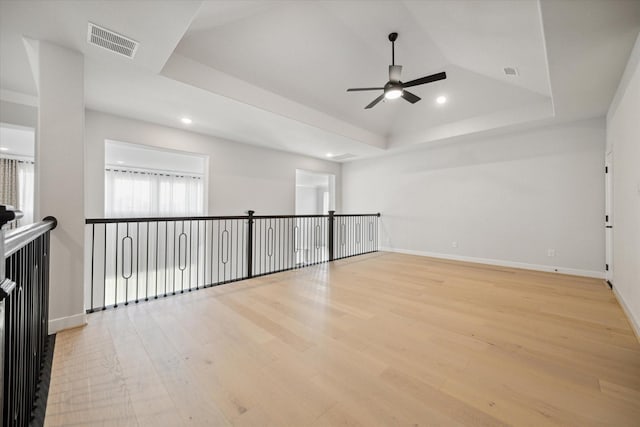 unfurnished room with ceiling fan, a tray ceiling, and light hardwood / wood-style floors