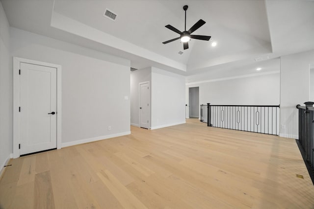 empty room with a raised ceiling, ceiling fan, lofted ceiling, and light hardwood / wood-style floors