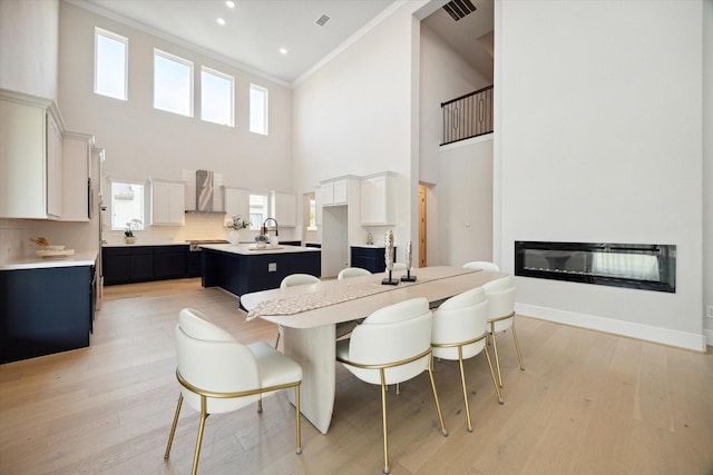 dining area featuring ornamental molding, sink, light wood-type flooring, and a towering ceiling