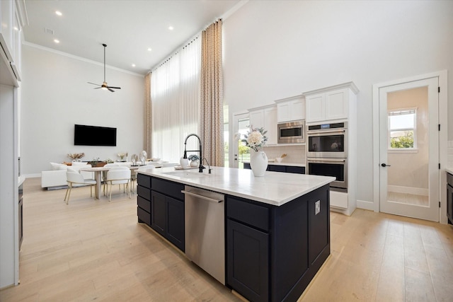 kitchen with sink, a kitchen island with sink, stainless steel appliances, light hardwood / wood-style floors, and white cabinets