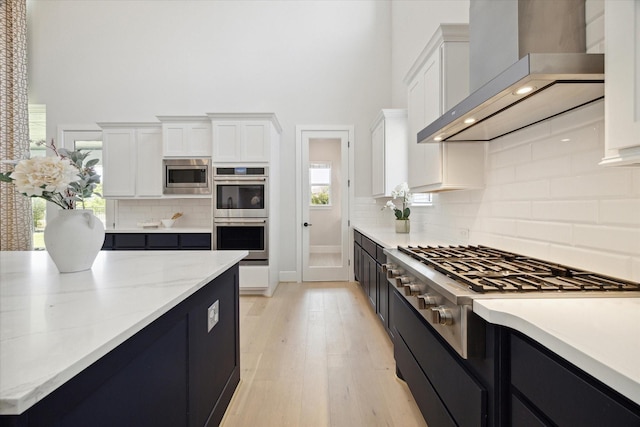 kitchen with wall chimney range hood, light hardwood / wood-style flooring, stainless steel appliances, and white cabinets